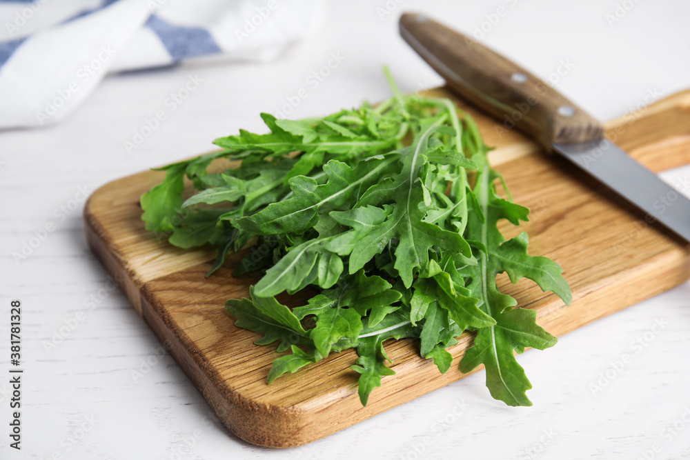Fresh arugula, cutting board and knife on white wooden table Fresh arugula, cutting board and knife on white wooden table