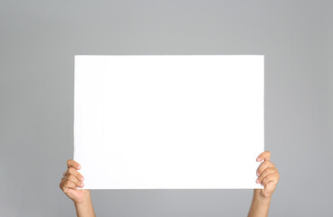 Man holding white blank poster on grey background, closeup. Mockup for design