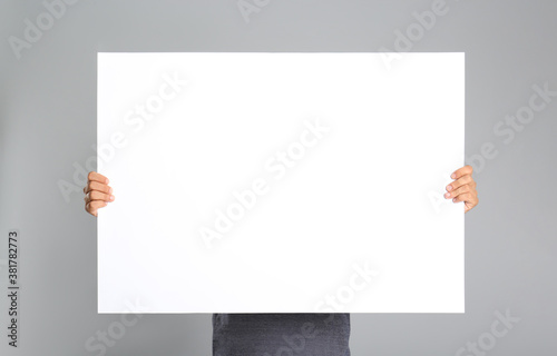 Man holding white blank poster on grey background. Mockup for design photo