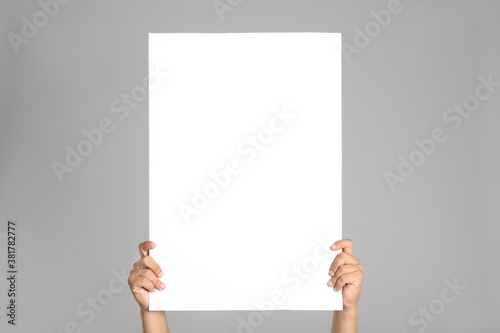 Man holding white blank poster on grey background, closeup. Mockup for design photo
