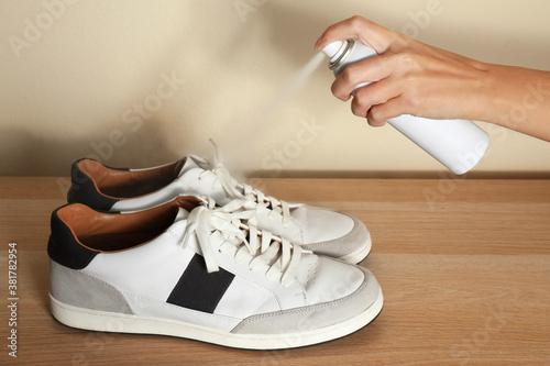 Foto Woman spraying deodorant over pair of shoes at home, closeup