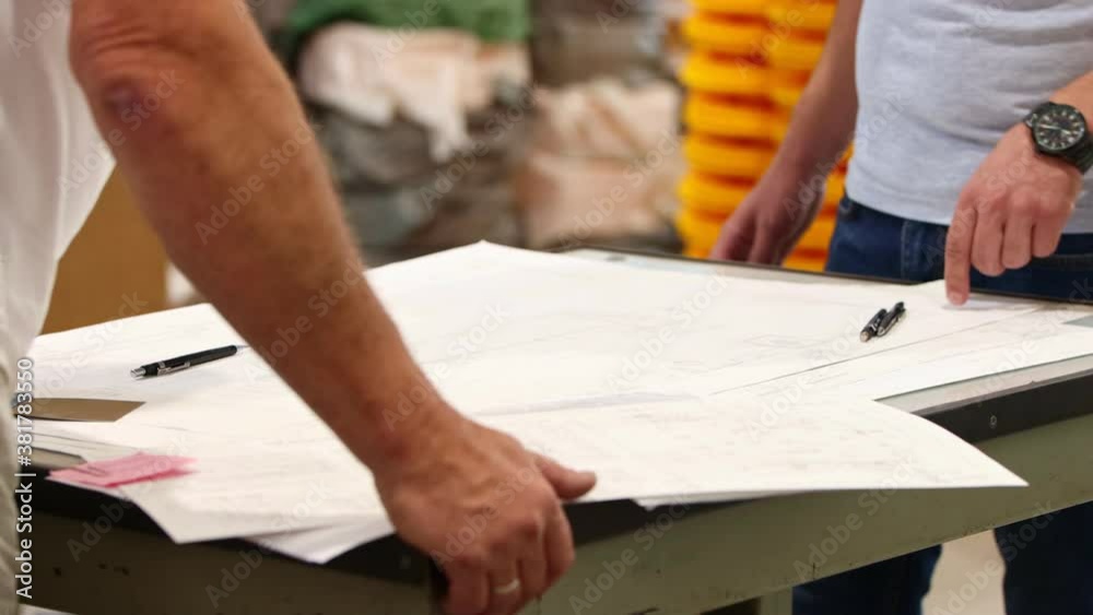 Men architectors standing above the plan on the paper and pointing at it Men architectors standing above the plan on the paper and pointing at it