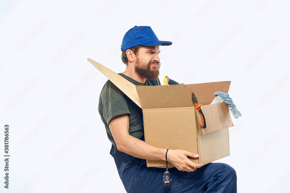 Worker man in uniform with a box in his hands tools delivery service light background Worker man in uniform with a box in his hands tools delivery service light background