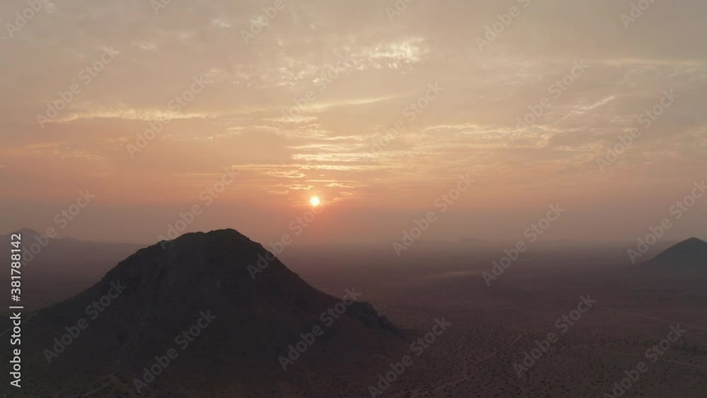 Arial view of a hazy orange sunset beyond a volcanic mountain in the Mojave Desert during wildfire season Arial view of a hazy orange sunset beyond a volcanic mountain in the Mojave Desert during wildfire season