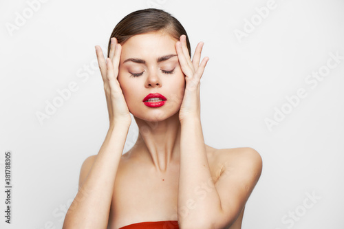 woman with bare shoulders With closed eyes, red lips are holding onto the face body care 