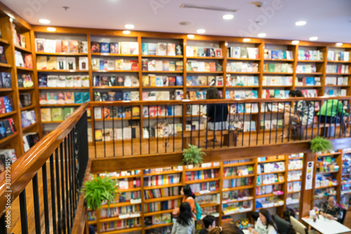 Blurred abstract background of bookshelves in book store, with a girl reading book in the store.