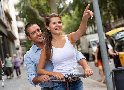 Portrait of happy young man and woman enjoying electro scooter riding in city