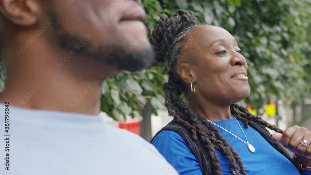 Older black female talking and laughing with a younger male relative on a bench outdoors Older black female talking and laughing with a younger male relative on a bench outdoors
