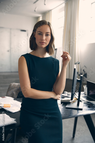 Young and beautiful female CEO business woman standing in front of desk at the office, looking confident and professional. Concept: female boss at office. 