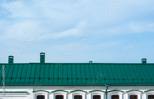 Green metal roof on a white brick building with metal chimneys against a blue sky