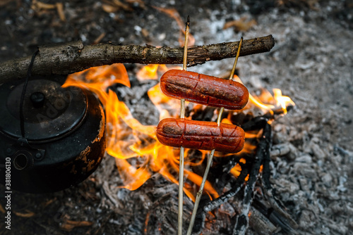 campfire sausage in pan, water bottle and titanium mug near the fire outdoors. bushcraft, adventure, travel, tourism and camping concept. photo