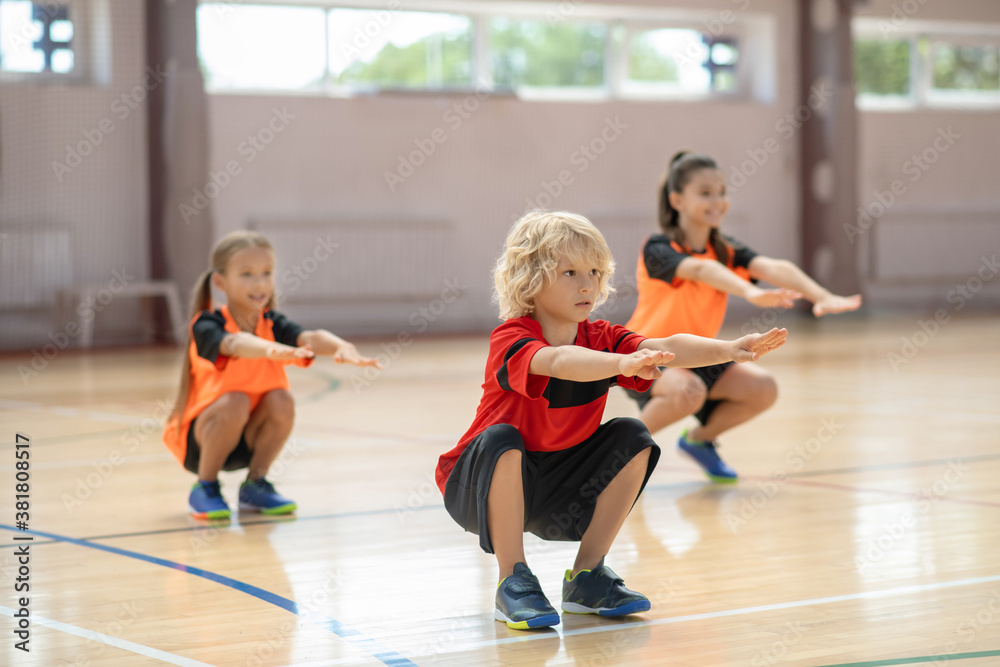 Three kids exercising in the gym and doing squats