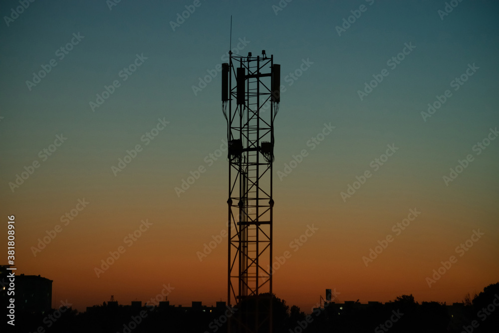 Silhouette of the mobile operator's antenna communication tower against the background of the evening orange-blue sky