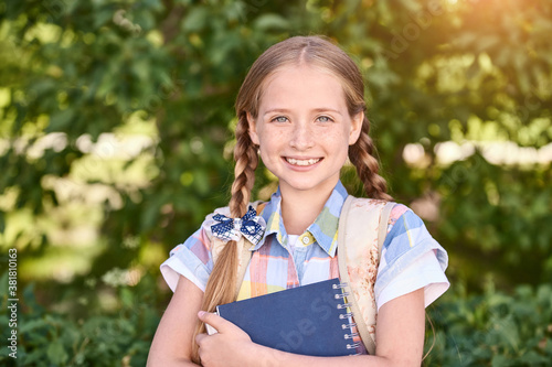 Beautiful american portrait of schoolgirl. Preschool kid. Little happy girl outdoors. Pretty female person. Adorable candid children. Park. Holding book. Smiling
