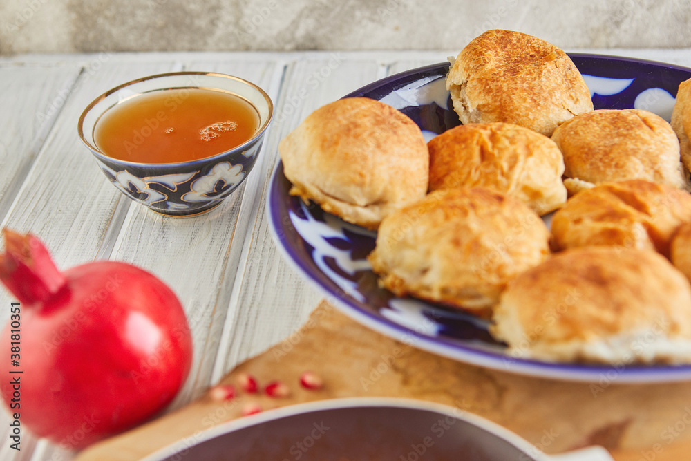 Asian baked meat pies - samsa or sambousak in a national plate with pomegranate, Middle Eastern cuisine on a wooden white table Asian baked meat pies - samsa or sambousak in a national plate with pomegranate, Middle Eastern cuisine on a wooden white table