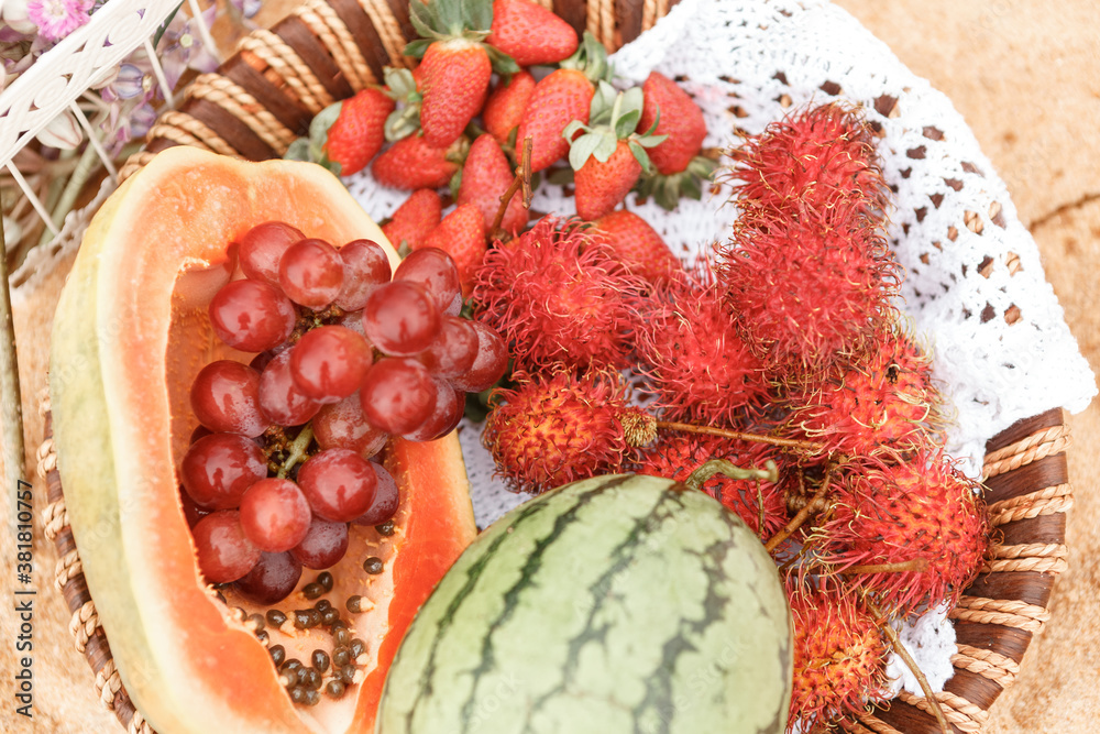 Picnic background with basket with tropical  fruits - watermelon, papaya, strawberries and rambutan on sandy bach