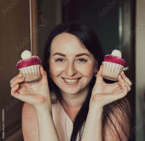 The girl holds delicious cupcakes with white cream in her hands  decorated balls with coconut powder. Holds cupcakes close to her face and smiles.