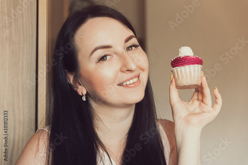 The girl holds delicious cupcake with white cream in her hands, decorated balls with coconut powder. Holds cupcake close to her face and smiles.