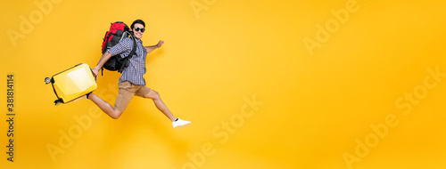 Young excited Caucasian male tourist with baggage jumping in mid-air isolated on colorful studio yellow banner background with copy space