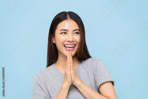 Smiling beautiful Asian woman doing Wai gesture for greeting or thank you isolated on light blue background photo