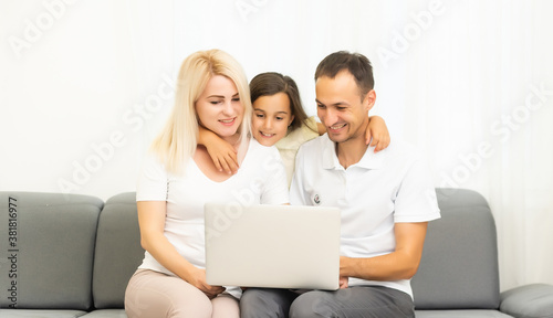 Happy family with kid girl having fun using laptop together sitting on sofa, parents and child daughter laughing relaxing at home with computer watching funny internet video, making online call