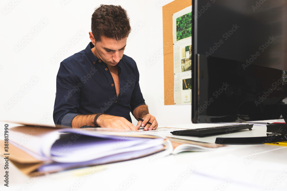 A young male architect working on a project in his office in Lisbon, Portugal. Young man working smart using the desktop computer while working on interior design project in his studio A young male architect working on a project in his office in Lisbon, Portugal. Young man working smart using the desktop computer while working on interior design project in his studio