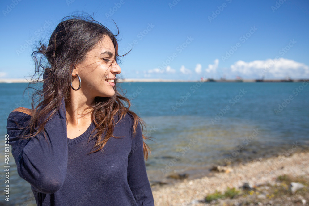 Profile of a young brunette italian woman with long hair and dark blue sweater by the sea romantic with hair in the wind is happy with deep blue sky