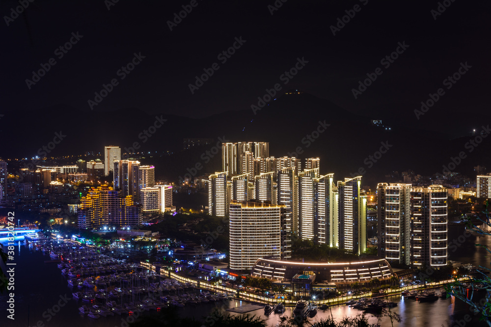 Naklejka premium Night view of Sanya city with bright multi-colored illumination buildings, structures, roads, sidewalks, poles, bridges.