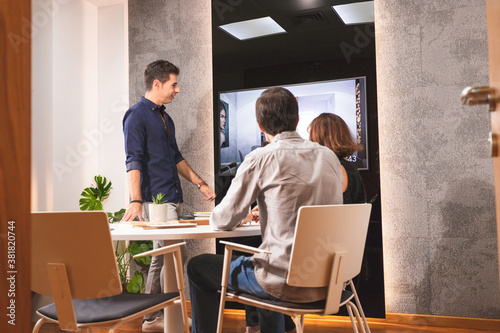 Three young architects discussing together inside a conference room the new interior design concept for a brand presentation. Young entrepreneurs working in team and looking at some project on a TV