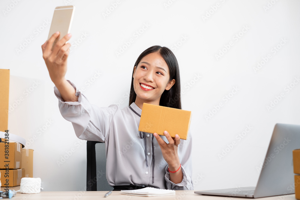 Young Asian woman business owner with many parcel boxes on the table happy online sales job, use your smartphone, get an order from customers, take notes, and make arrangements for delivery by post Young Asian woman business owner with many parcel boxes on the table happy online sales job, use your smartphone, get an order from customers, take notes, and make arrangements for delivery by post