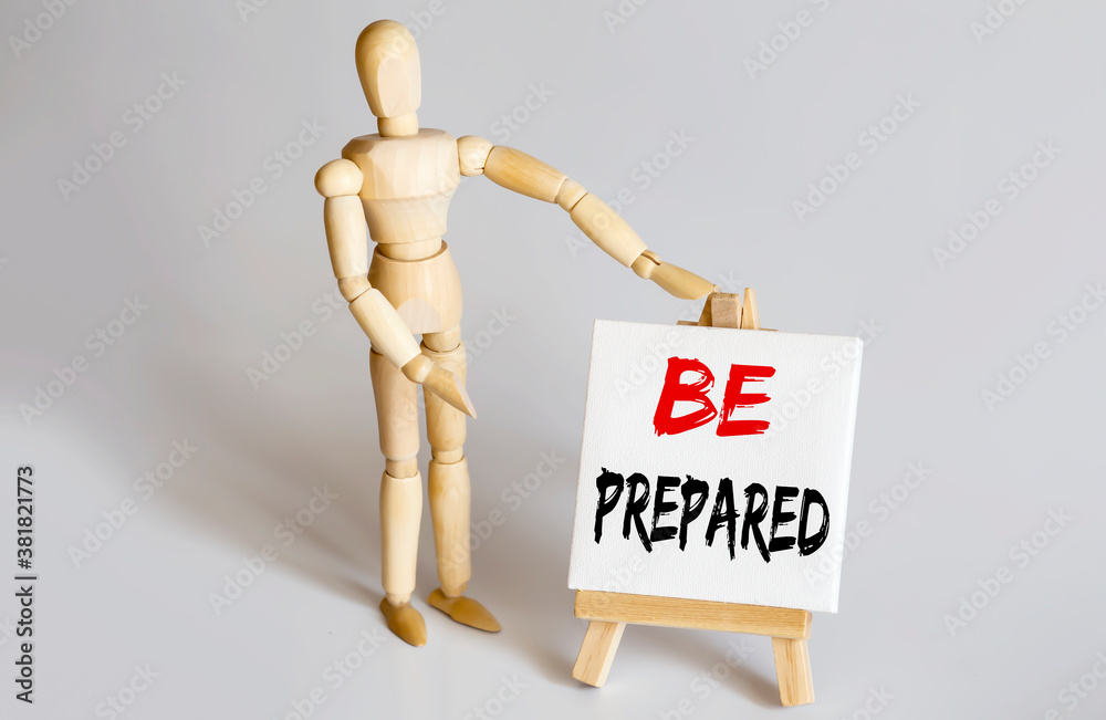 Wooden man shows with a hand to white easel with text BE PREPARED on white background Wooden man shows with a hand to white easel with text BE PREPARED on white background