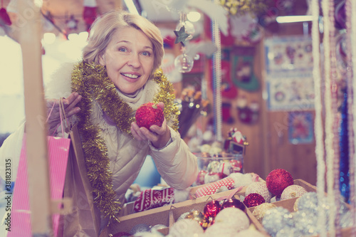 Smiling woman choosing Christmas toys at Christmas market and walking