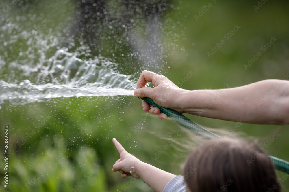 Details with the hands of a senior woman and her granddaughter watering the garden with a hose.