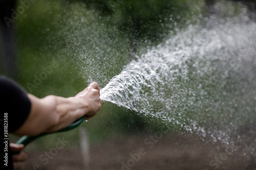 Details with the hand of a senior woman watering her rural garden with a hose.