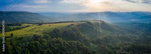 Fototapeta Naklejka Na Ścianę i Meble -  Early morning in the mountains. Morning sun and haze in the valley against the background of mountains. Mountain summer landscape. Banner size