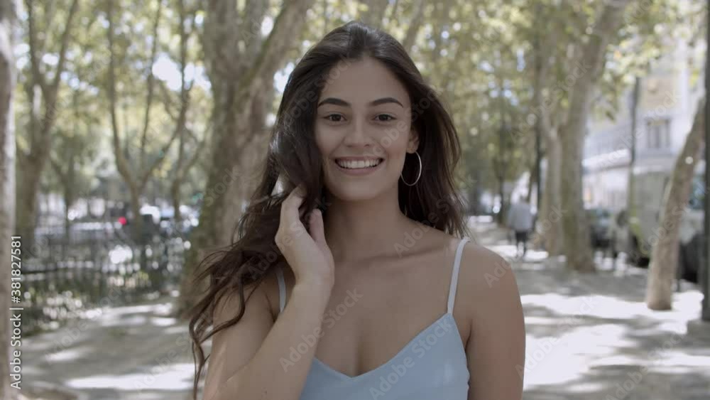 Portrait of young brunette woman standing on street, smiling and posing for photo. Happy beautiful Caucasian female model in city park looking at camera. Front view. Appearance and expression concept Portrait of young brunette woman standing on street, smiling and posing for photo. Happy beautiful Caucasian female model in city park looking at camera. Front view. Appearance and expression concept