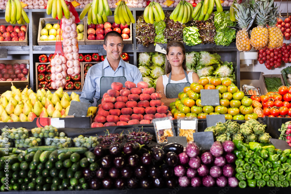 Friendly and young man and woman vegetable shop sellers posing behind counter