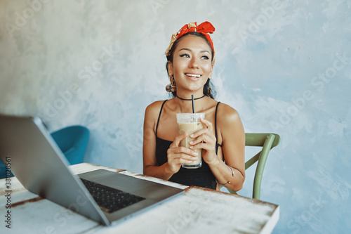 Obraz na płótnie a young mixed race woman drink iced coffee and using her laptop in cafe w salonie
