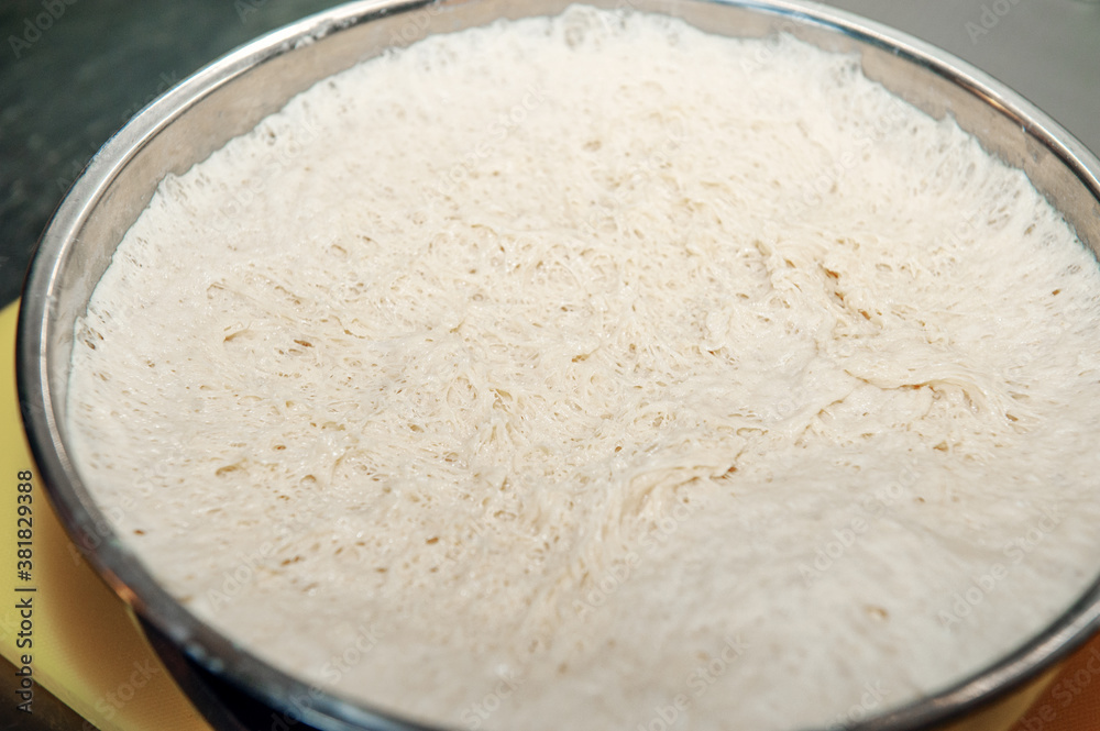Pulling the plastic wrap off the raised bread dough in a metal mixing bowl. The gluten is stretched, showing that the raw flour mixture can be formed into a loaf and baked. Pulling the plastic wrap off the raised bread dough in a metal mixing bowl. The gluten is stretched, showing that the raw flour mixture can be formed into a loaf and baked.