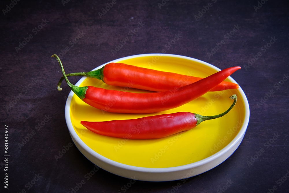 Red chilli pepper on yellow plate in dark background