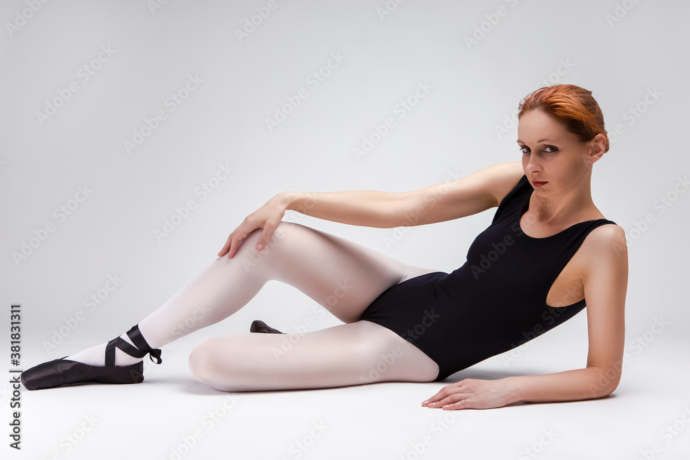 Relaxing Caucasian Professional Ballet Dancer in Body Suit and Pointes Shoes Posing Against White Background. Relaxing Caucasian Professional Ballet Dancer in Body Suit and Pointes Shoes Posing Against White Background.