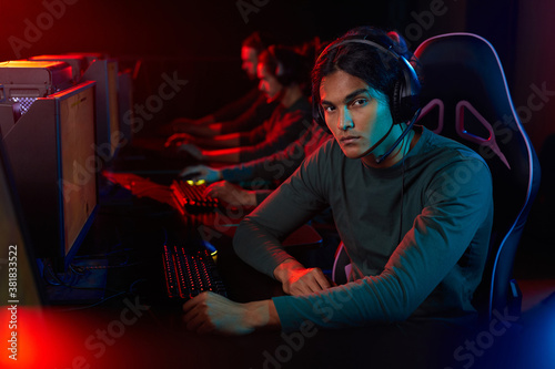 Portrait of young man looking at camera while sitting on chair in front of computer and playing game