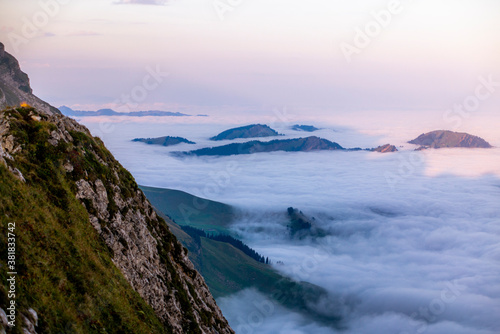 Colorful sunrise on the clouds and steep ridge of the majestic Schaefler peak in the Alpstein mountain range Appenzell, Switzerland with the fog in the valley rolling over the hills