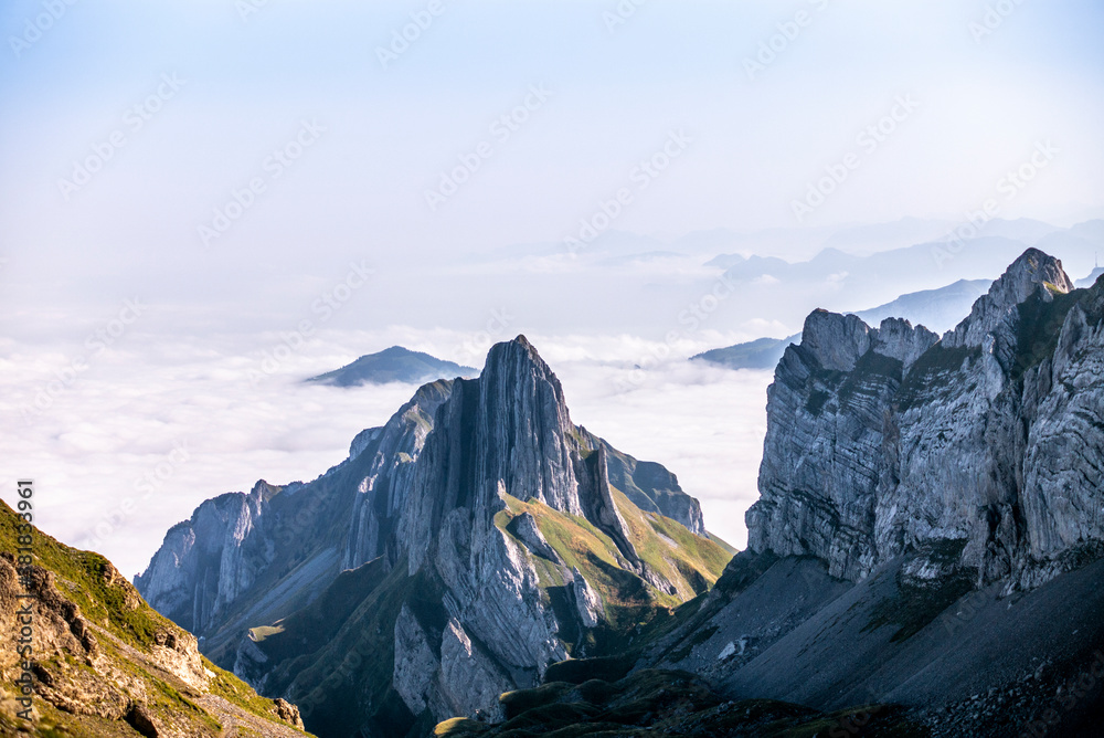 Colorful sunrise on the clouds and steep ridge of the majestic  Schaefler peak in the Alpstein mountain range Appenzell, Switzerland with the fog in the valley rolling over the hills