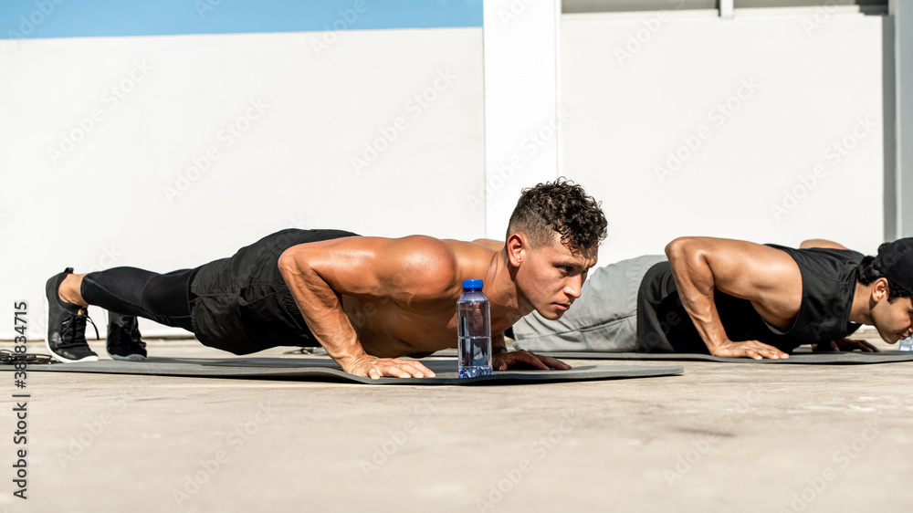 Group of fit male bodybuilders doing bodyweight push up exercise outdoors on building rooftop