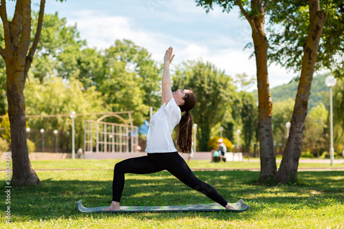 Yoga. A young woman in sportswear stands in a warrior's asana, doing yoga in a Park on the grass. The concept of healthy lifestyle and sports. Side view