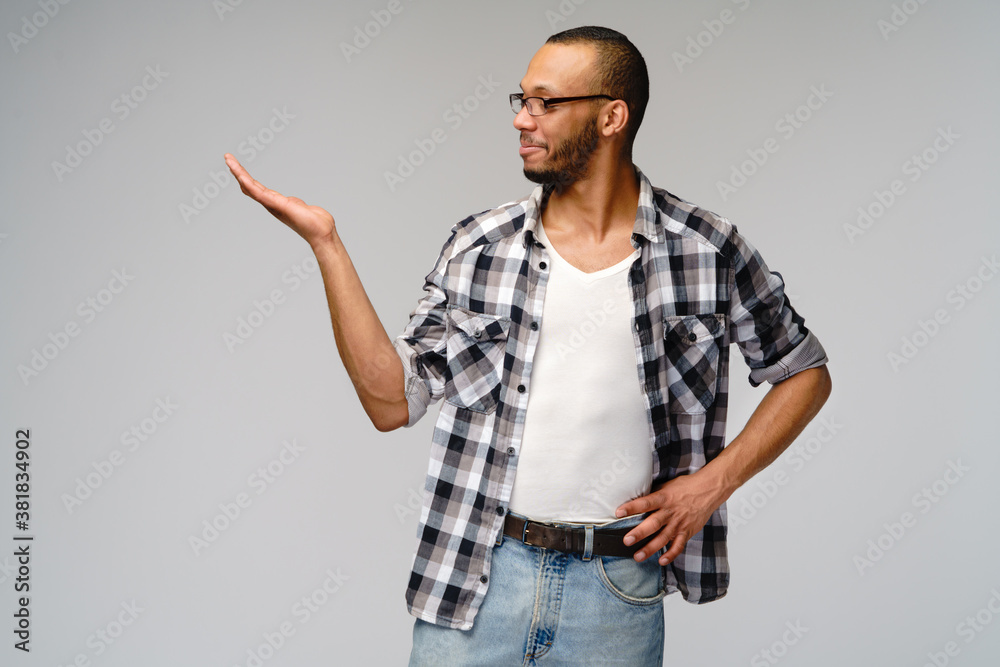 Joyful friendly african-american young man iwearing casual shirt pointing by finger at copy space Joyful friendly african-american young man iwearing casual shirt pointing by finger at copy space