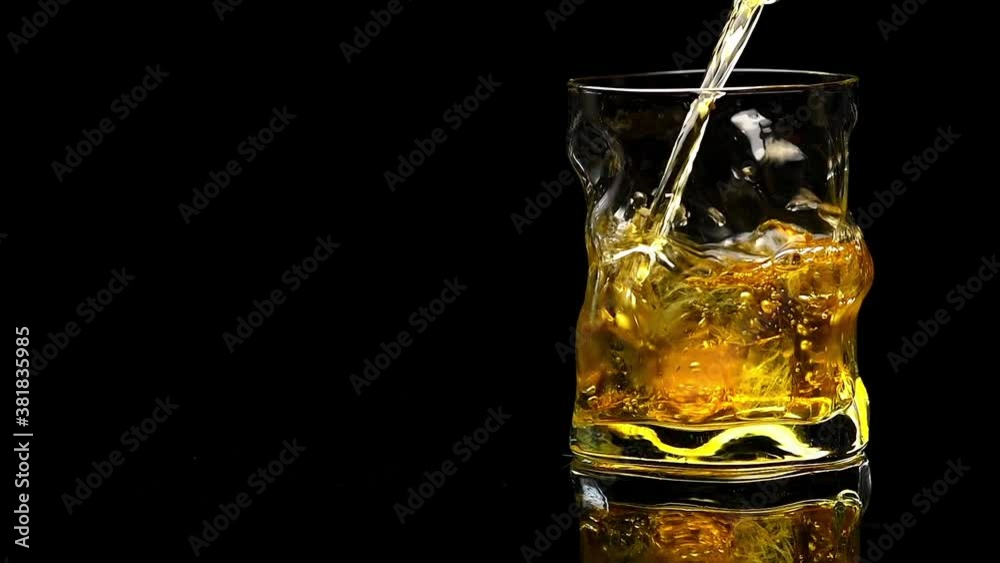 whiskey is poured into a crystal glass with ice on a black background whiskey is poured into a crystal glass with ice on a black background