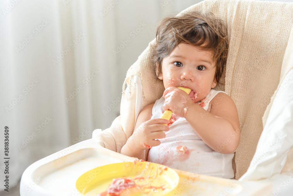Messy baby girl eating cake. Lovely infant girl holding a spoon, enjoying eating cake. Messy baby girl eating cake. Lovely infant girl holding a spoon, enjoying eating cake.