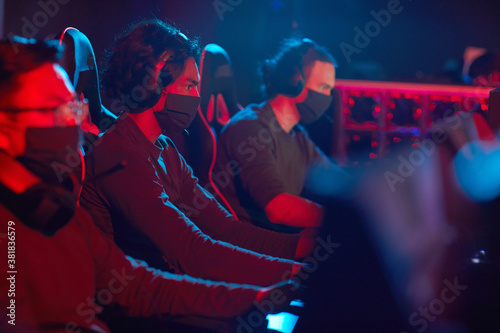 Group of young men in masks playing computer games in dark room in computer club